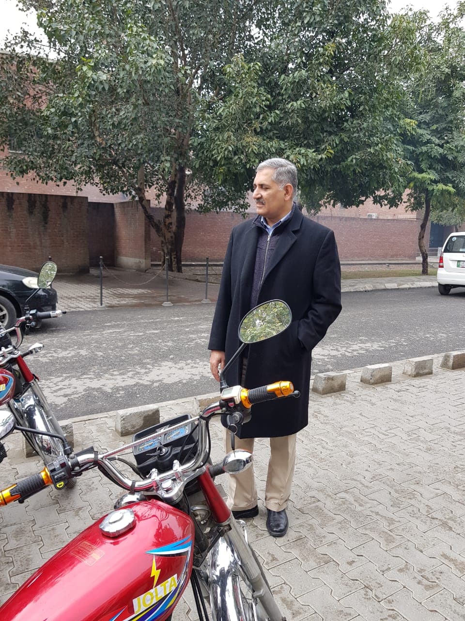 A LUMS professor standing beside a Jolta electric motorcycle on campus